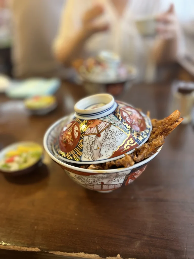 A tendon bowl partly covered with a decorative lid and tempura visible at the side