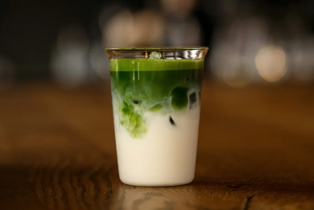 Iced matcha latte layered with milk on a wooden counter