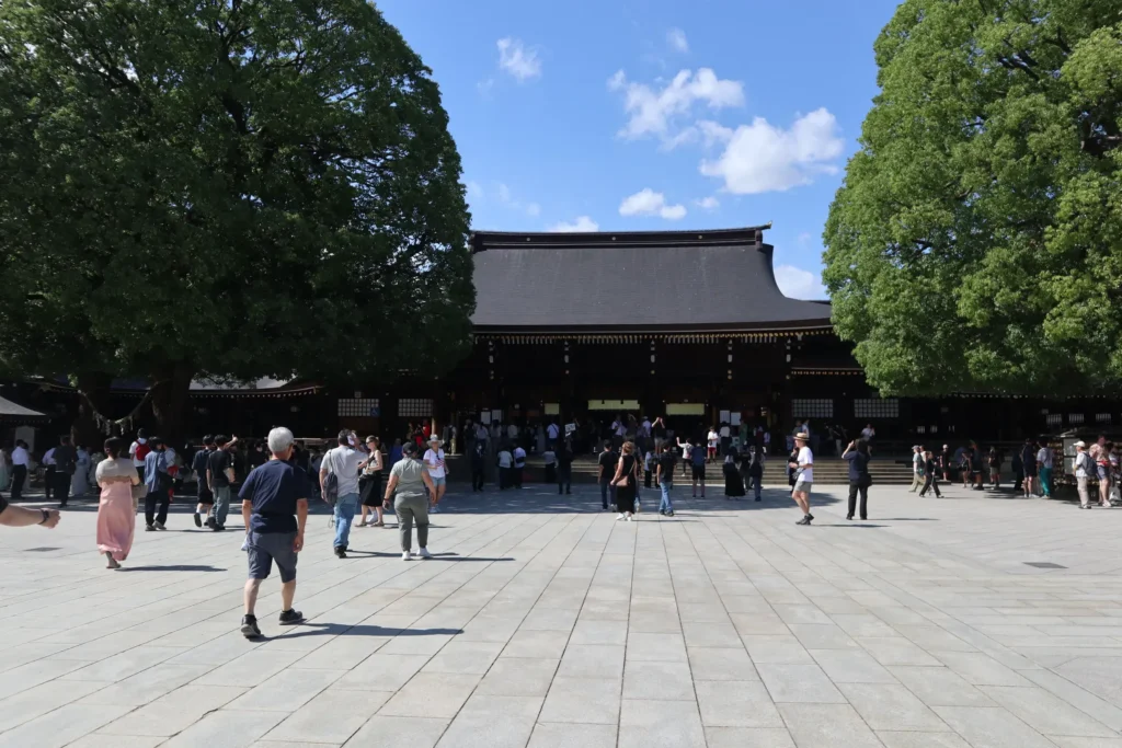 Visitors walking across the courtyard toward a shrine building surrounded by large trees