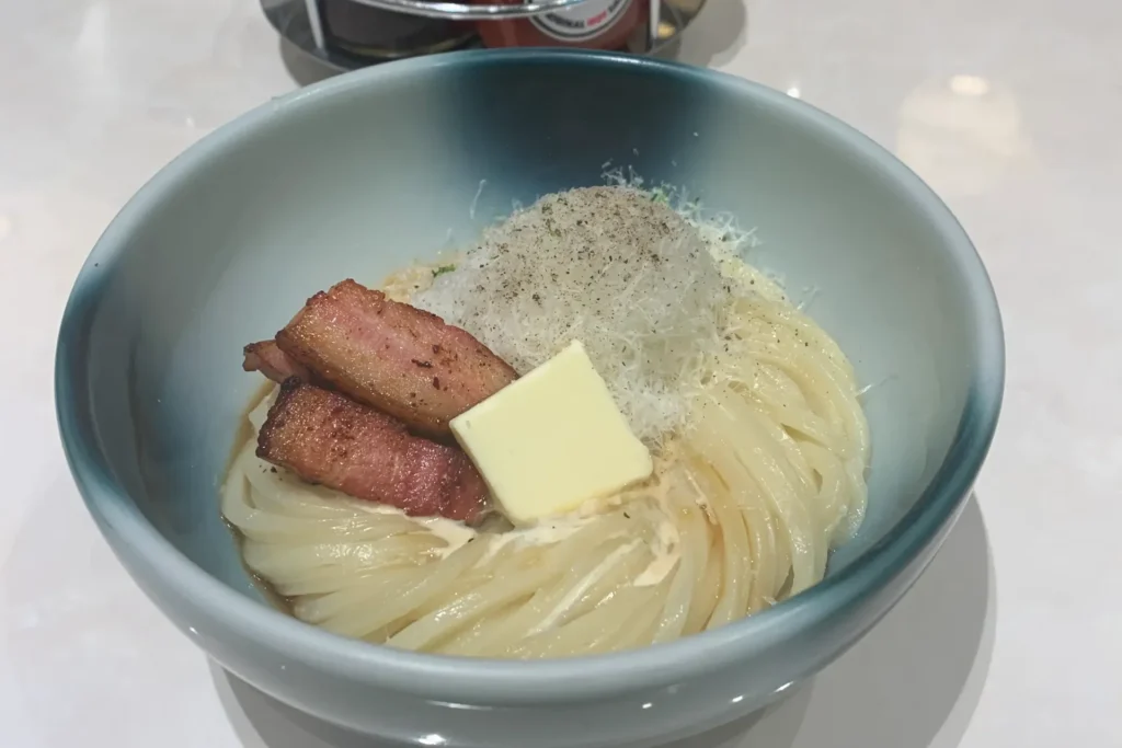 Creamy carbonara udon topped with bacon, butter, cheese, and black pepper at Mensho