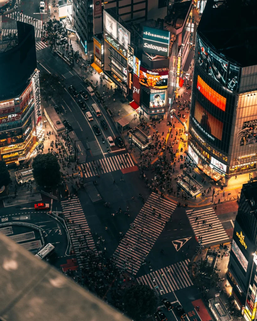 Aerial nighttime view of Shibuya Crossing with bright signs and pedestrian crossings