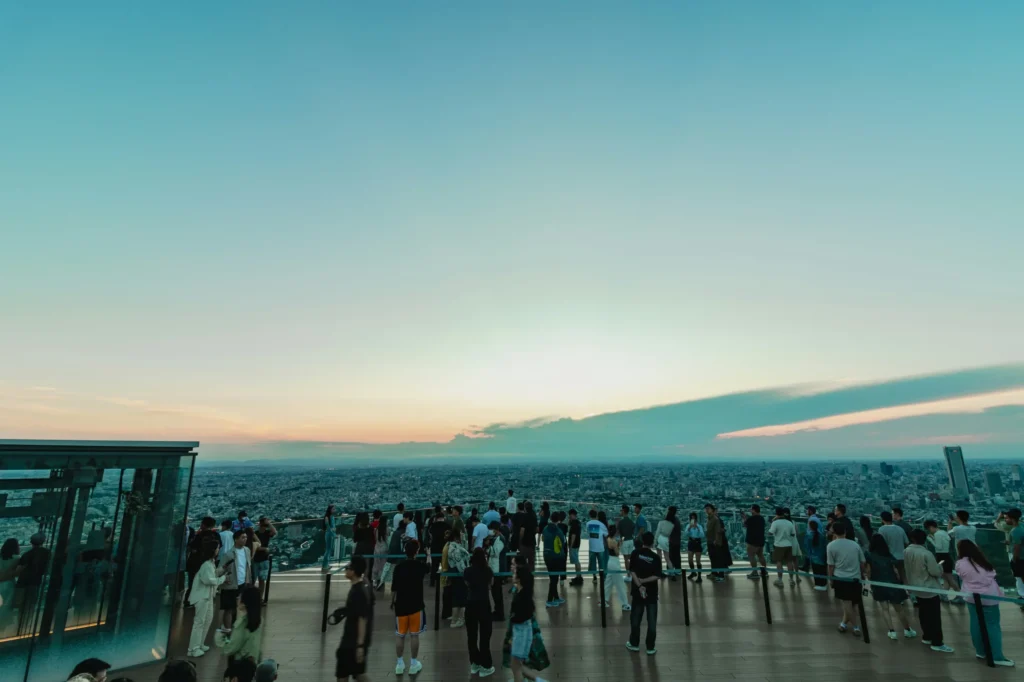 Visitors standing on an open rooftop observation deck overlooking Tokyo at sunset