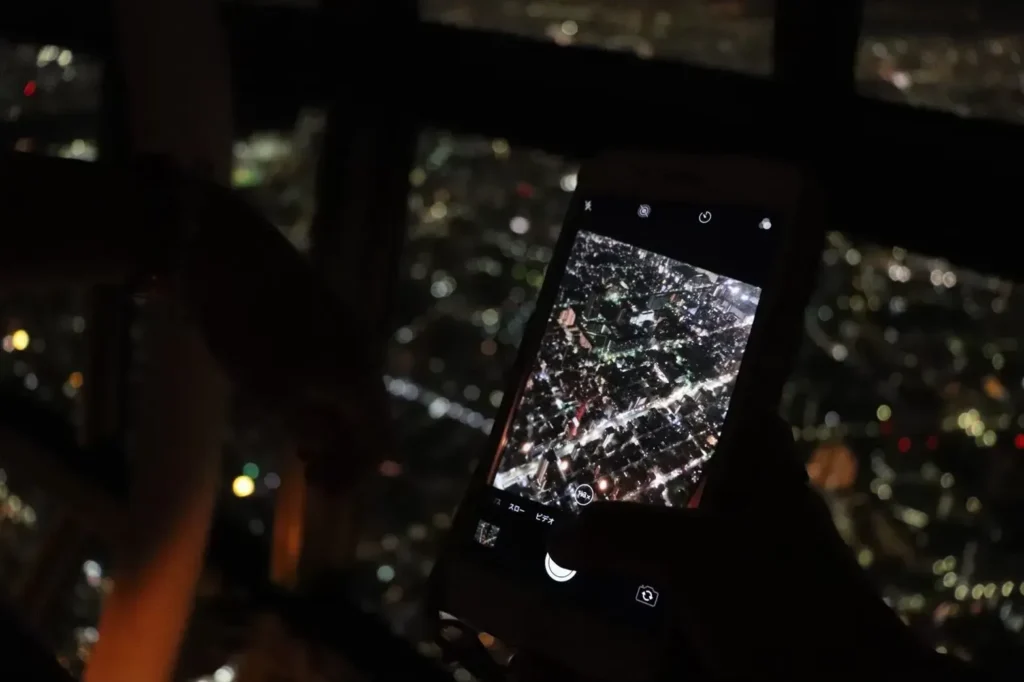 A smartphone camera pointed at the nighttime city view from an observation deck