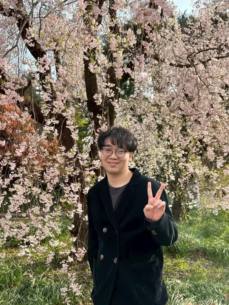 Visitor standing beneath pink weeping cherry blossoms in Shinjuku Gyoen